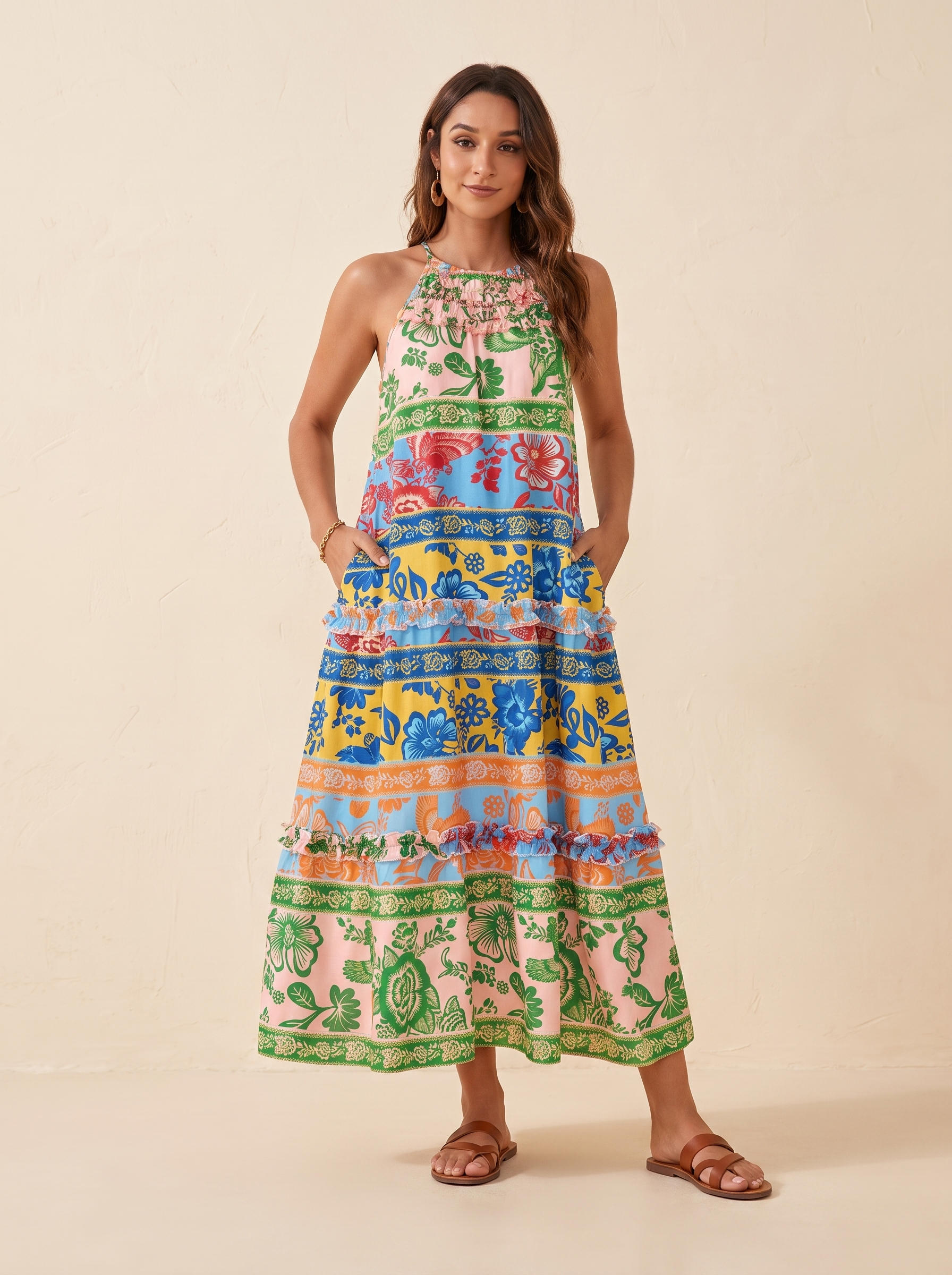 A woman modeling a sleeveless, tiered maxi dress with a vibrant, multicolored bohemian-style print featuring animals and floral motifs, set against a plain beige studio background.